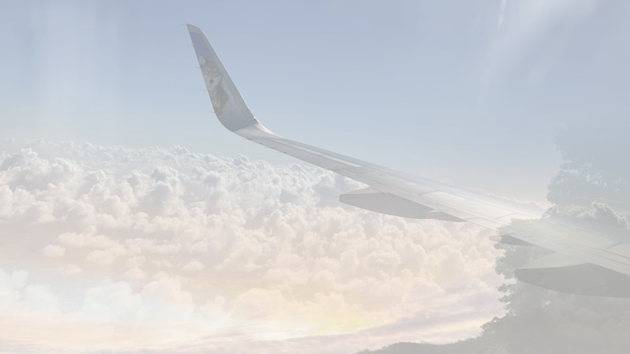 Airplane wing above sunlit clouds at golden hour